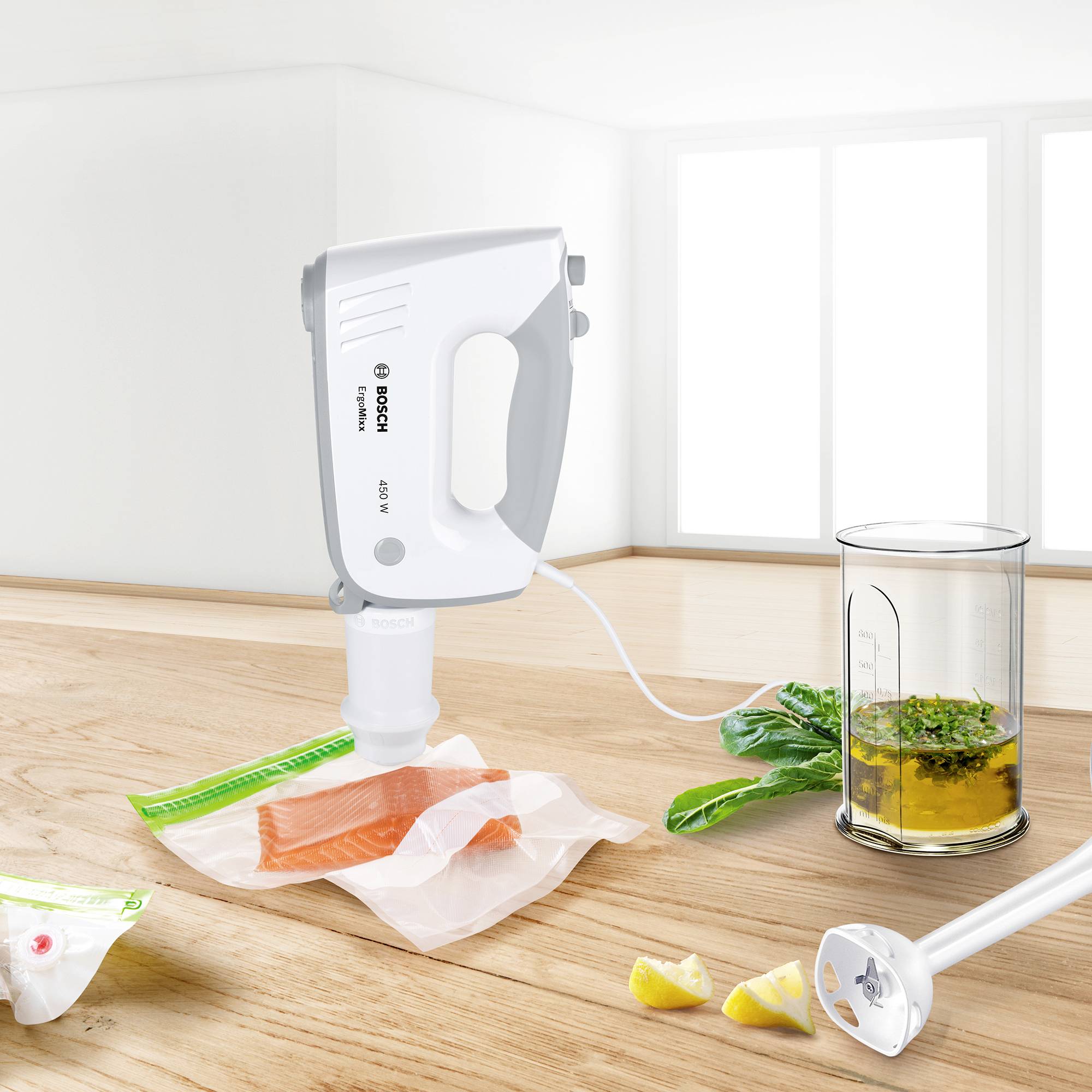 Batteur électrique et accessoires sur une table en bois, filet de saumon dans un sachet sous vide, roquette et herbes dans un verre doseur. Fenêtre en arrière-plan.