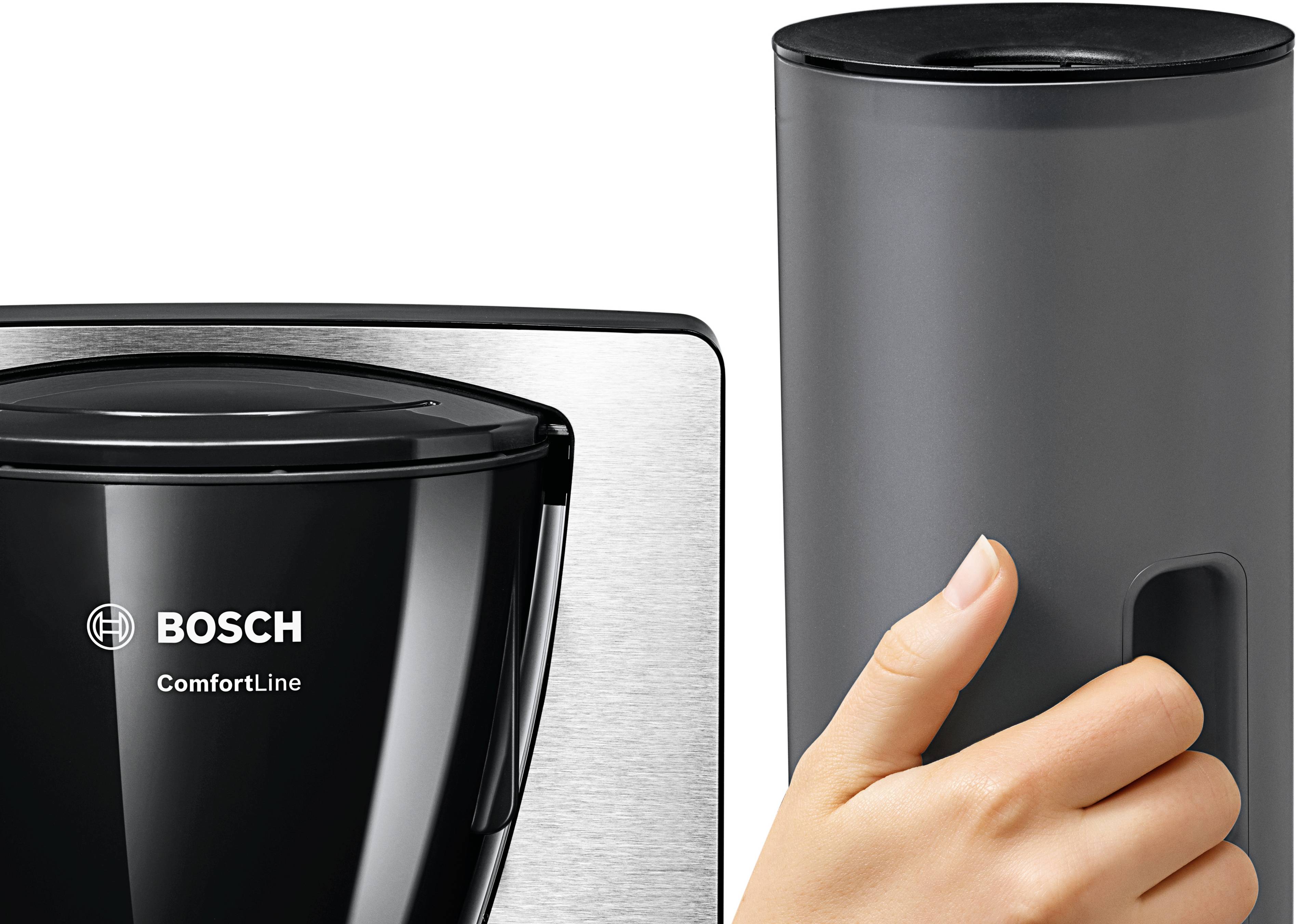 Une main tient un récipient cylindrique gris à côté d'une machine à café Bosch ComfortLine noire avec des éléments en acier inoxydable.