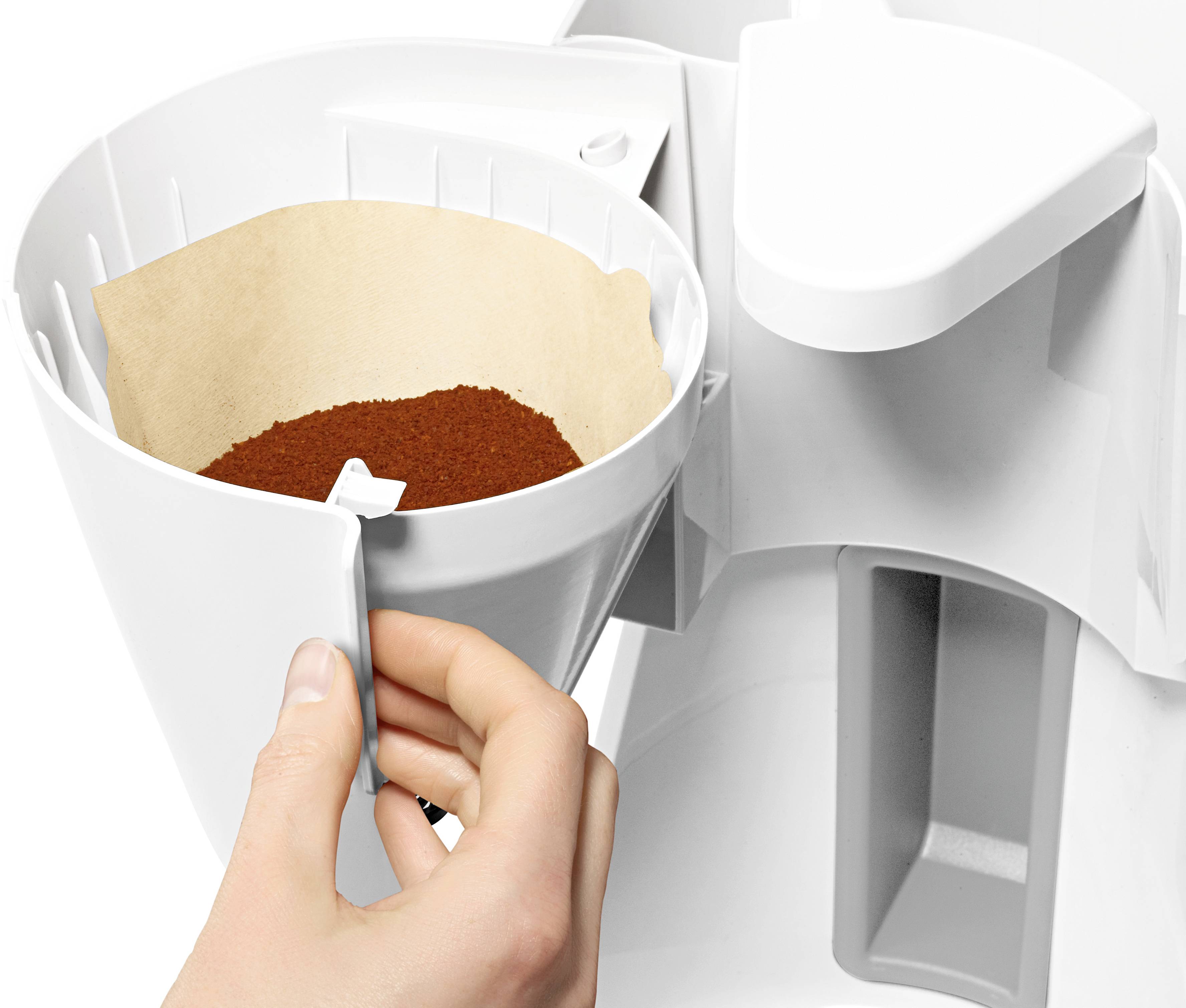 Une main tient un porte-filtre de machine à café rempli de poudre de café. La machine est blanche.