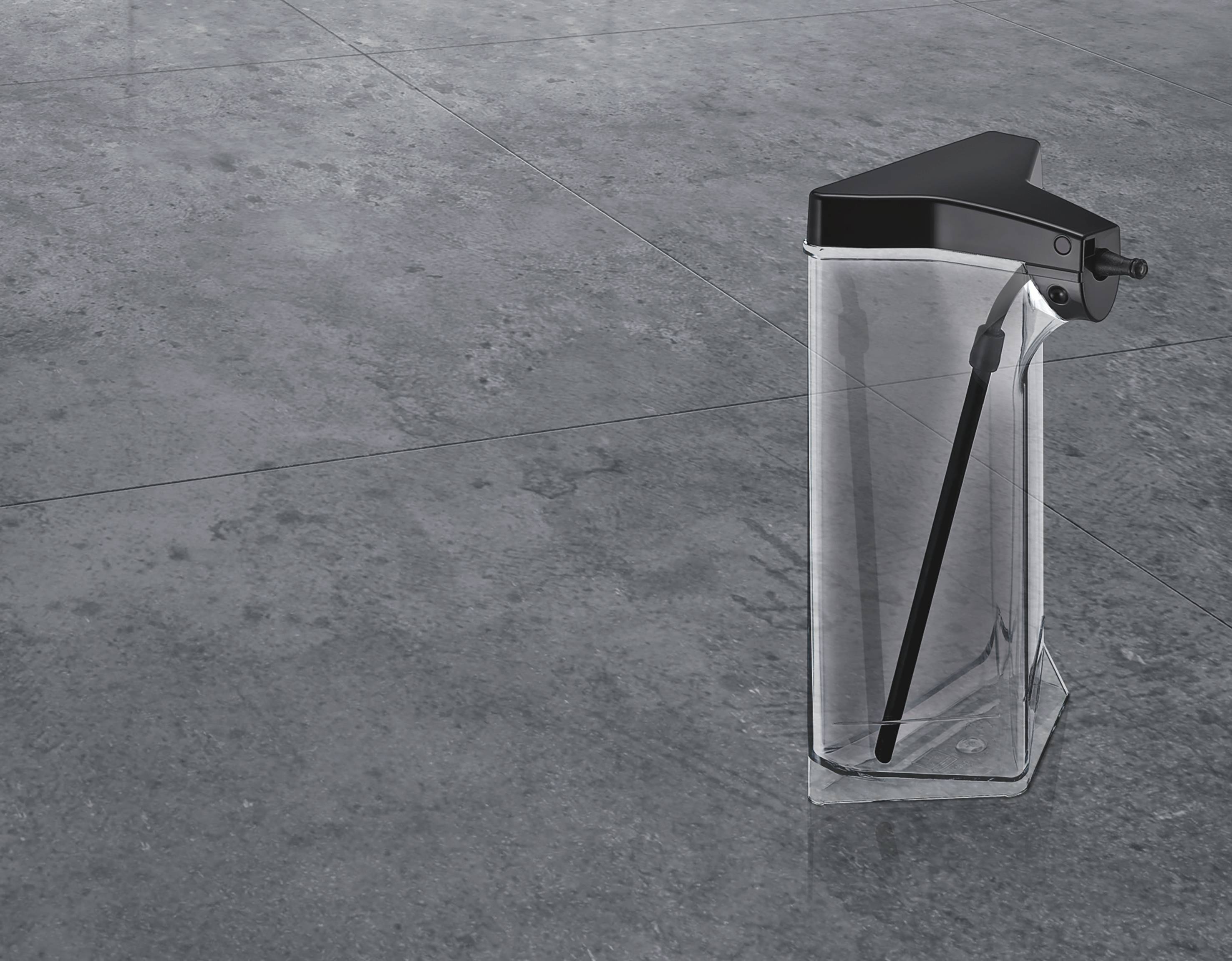 Une pompe à liquide transparente avec un couvercle noir est posée en diagonale sur un sol carrelé gris, prête à fonctionner.