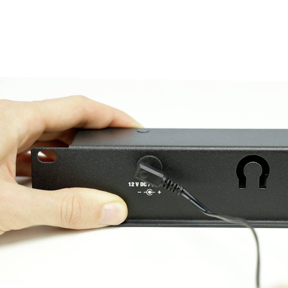 Une main tient un appareil électrique avec un câble DC 12 V connecté. Un trou de serrure pour la fixation murale est visible.