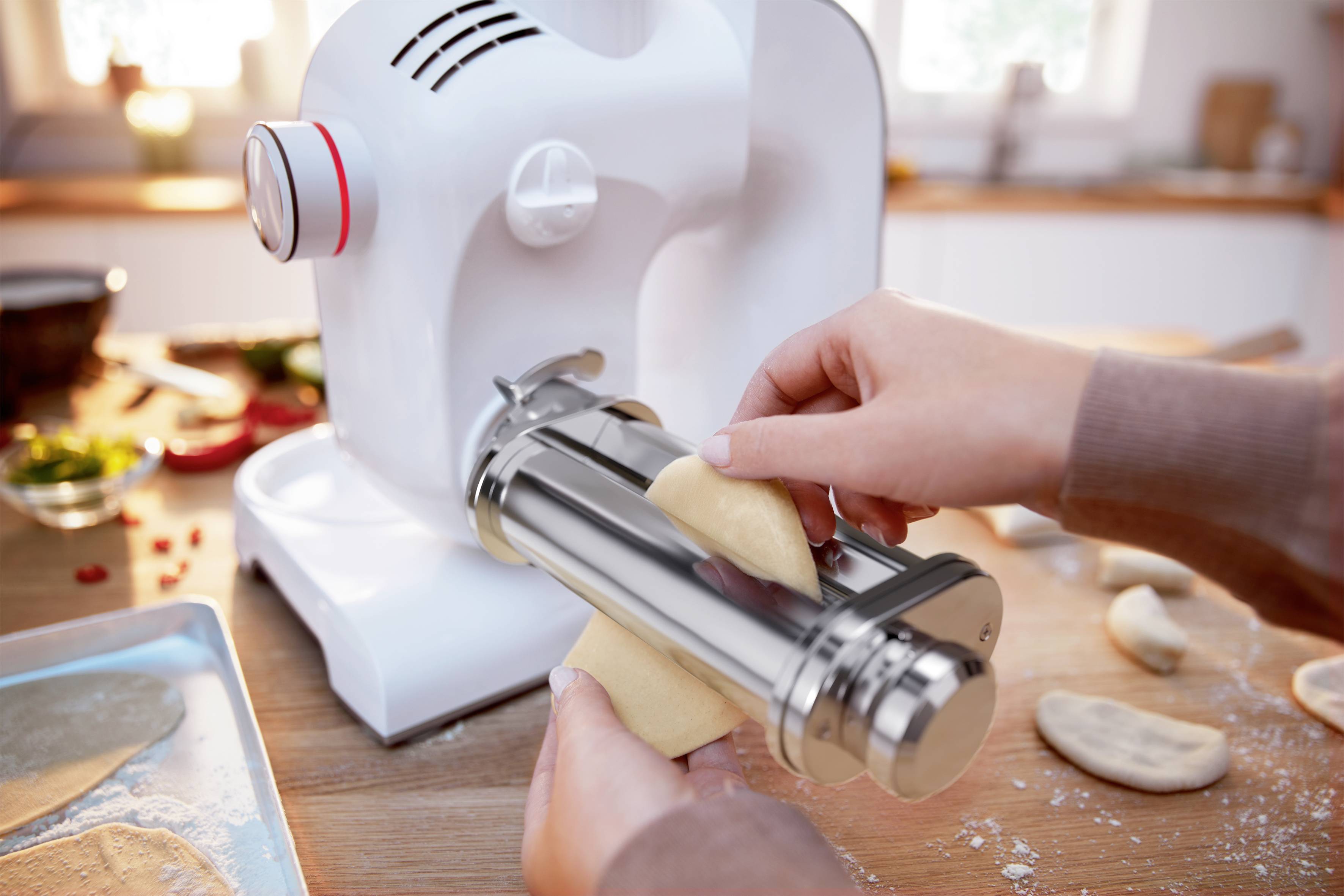 Une personne forme une pâte à l'aide d'un robot de cuisine sur un plan de travail. L'environnement montre des ingrédients et des pièces de pâte déjà préparées.
