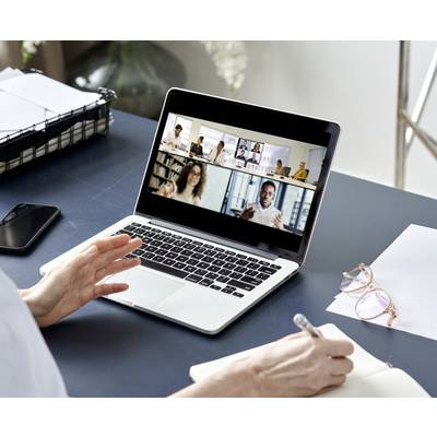 Une personne participe à une réunion virtuelle sur un ordinateur portable avec plusieurs participants. Des notes sont prises sur un bloc-notes.