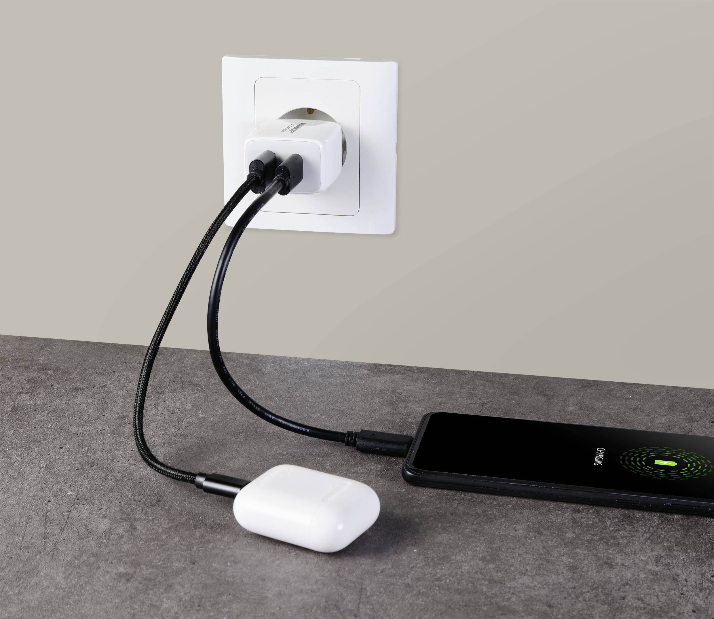 Un smartphone et des écouteurs sans fil sont chargés par le même chargeur à une prise murale.