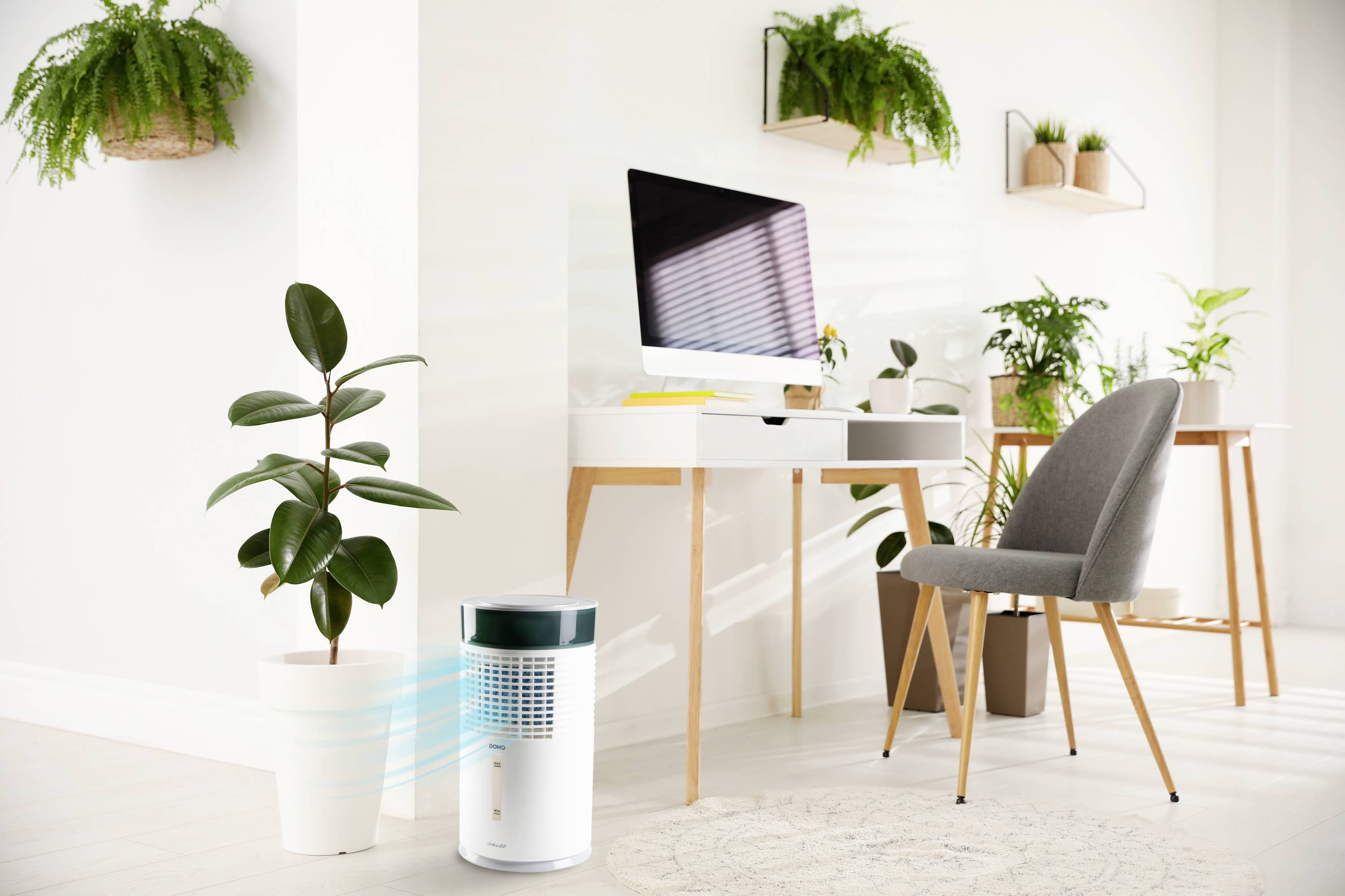 Purificateur d'air à côté d'une plante en pot dans un bureau moderne et lumineux avec un ordinateur sur le bureau, éclairé par la lumière du soleil à travers les persiennes.