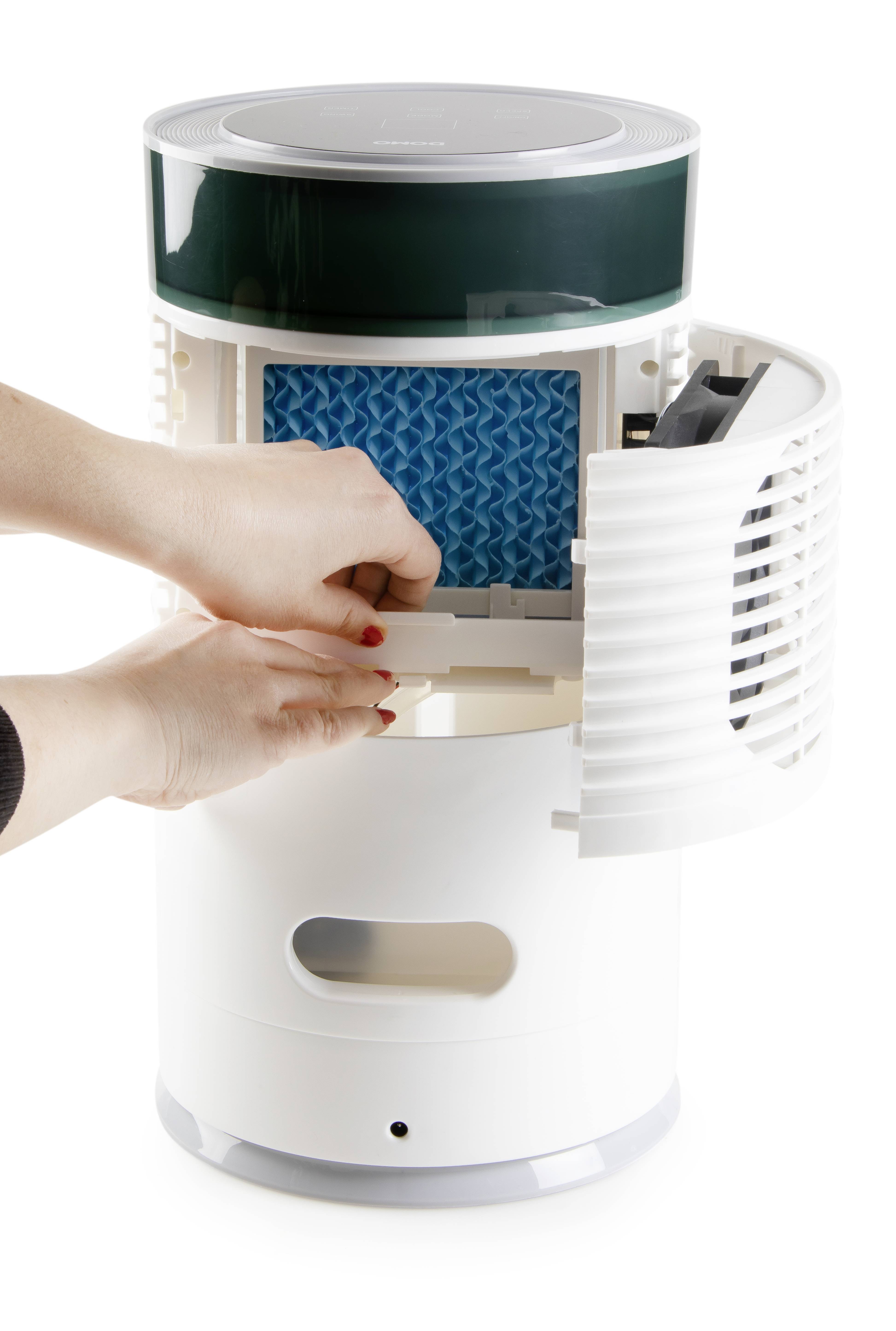 Une personne change le filtre d'un purificateur d'air. Le purificateur d'air est cylindrique et blanc, avec un compartiment ouvert dans lequel le filtre est inséré.