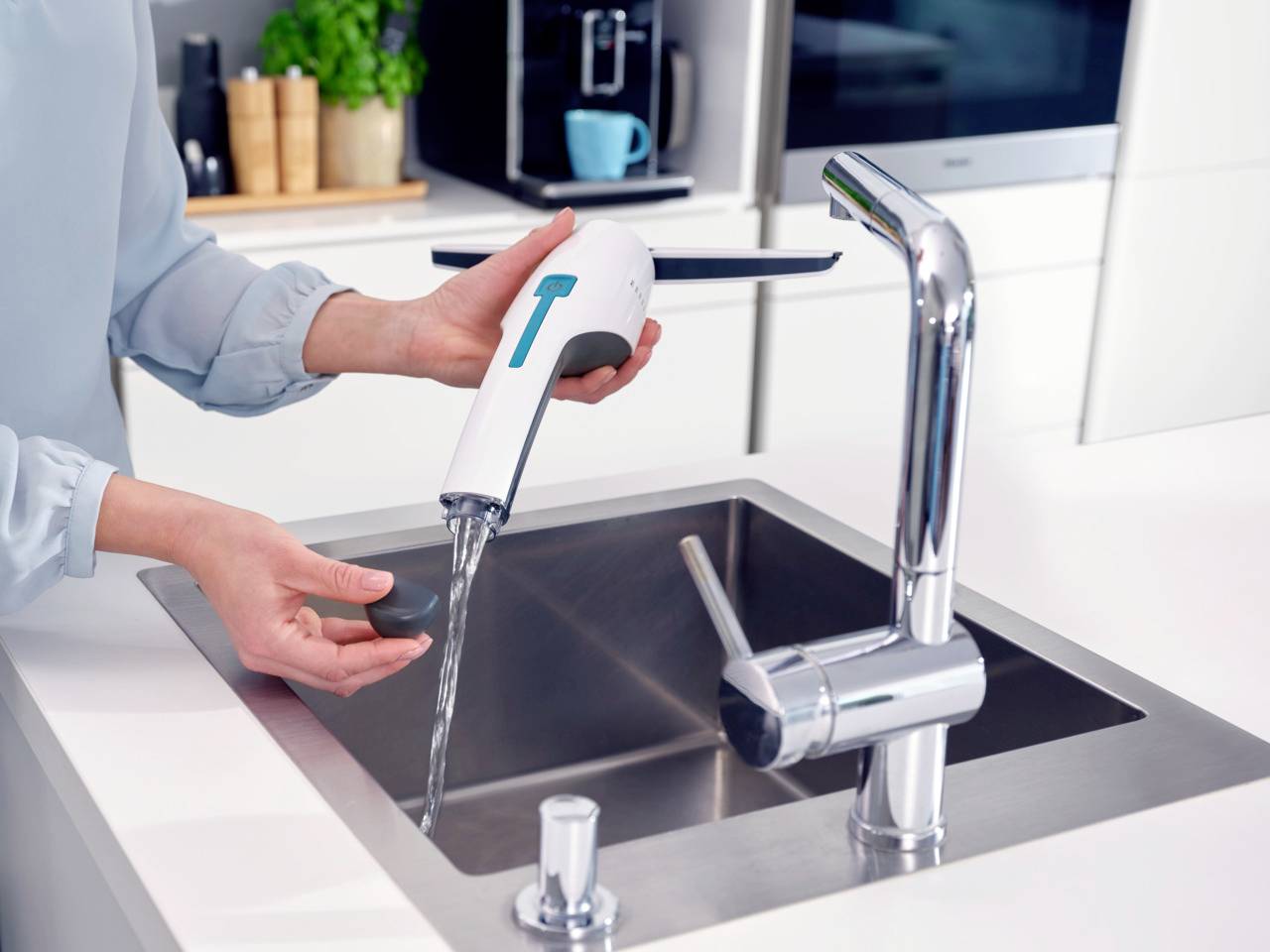 Une personne nettoie un éponge avec un nettoyeur de vitres électrique au-dessus d'un évier de cuisine. Une machine à café est visible en arrière-plan.