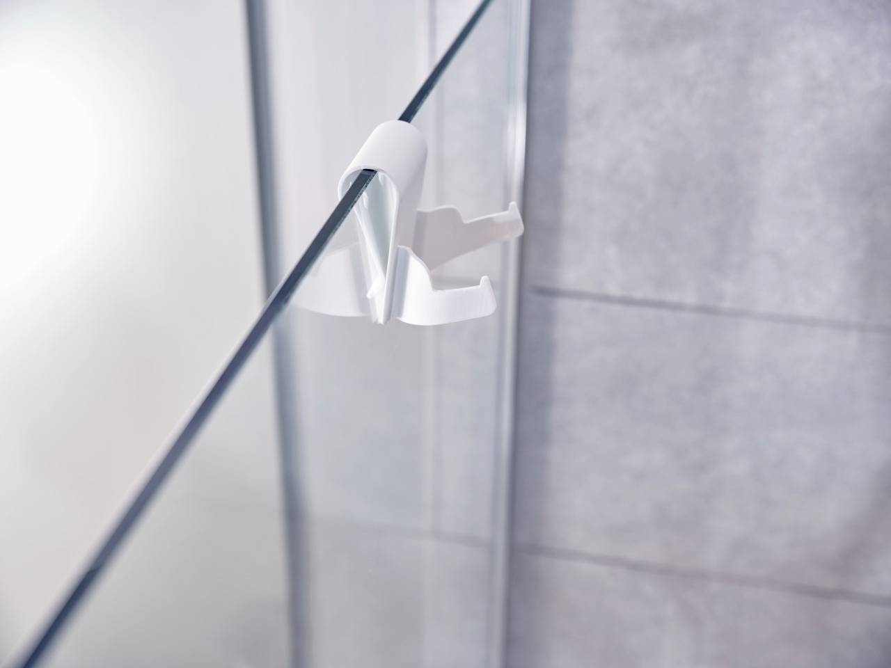 Un collier de serrage blanc fixe une paroi de verre dans une salle de bain moderne avec des carreaux gris en arrière-plan.