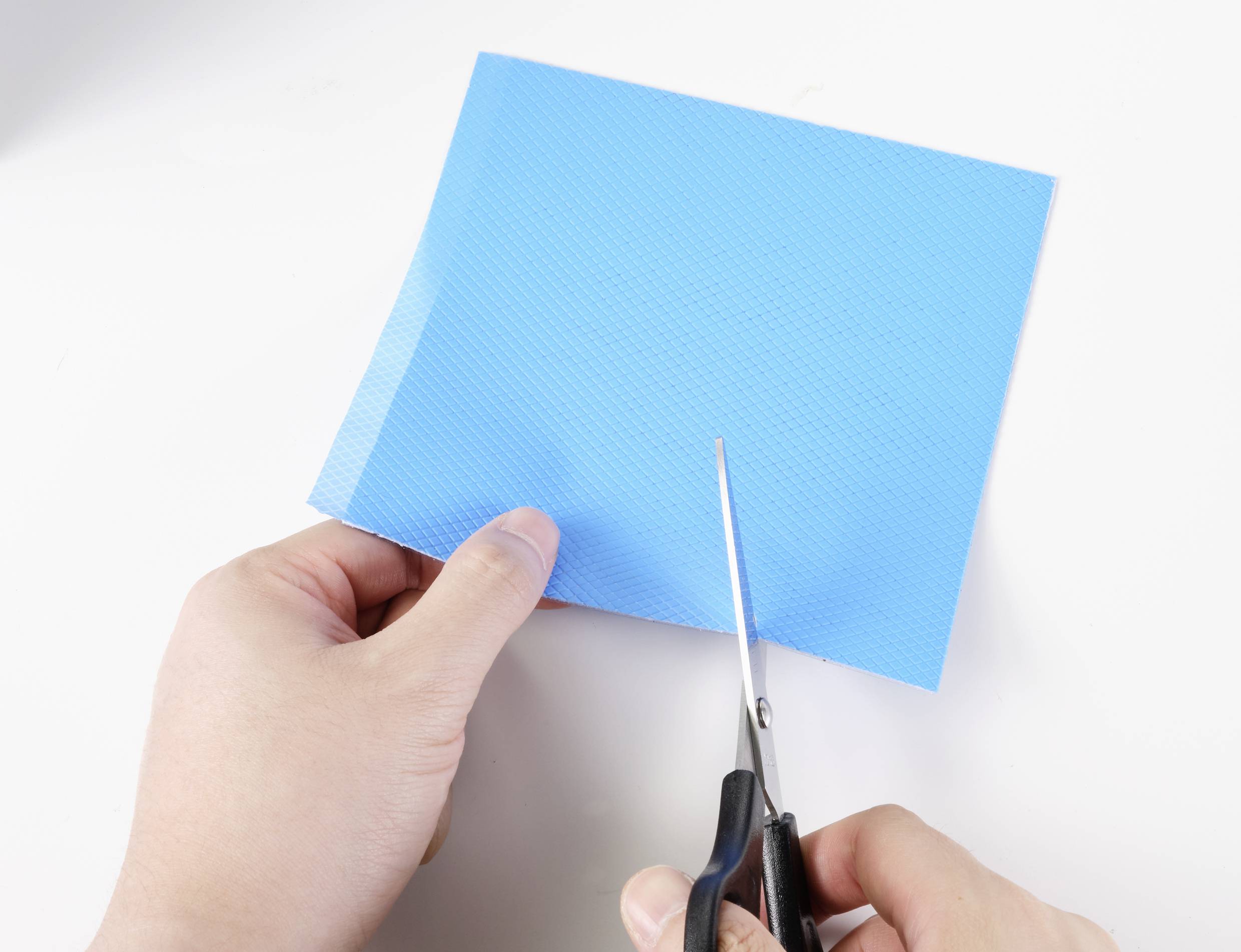 Une personne coupe un morceau de papier bleu avec des ciseaux sur un fond blanc.