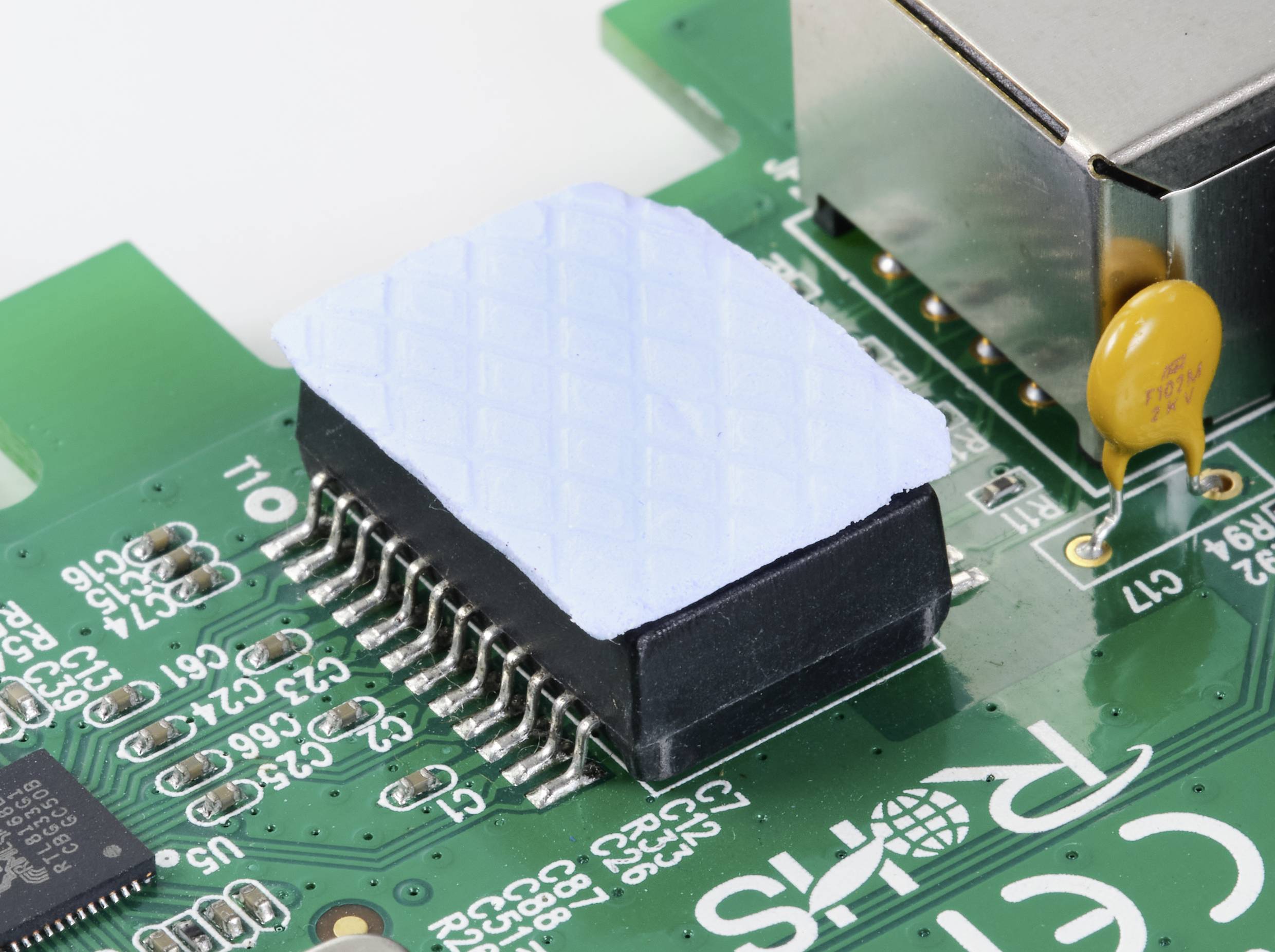 Un gros plan d'une carte électronique verte avec un circuit intégré, partiellement recouvert par un dissipateur thermique bleu.