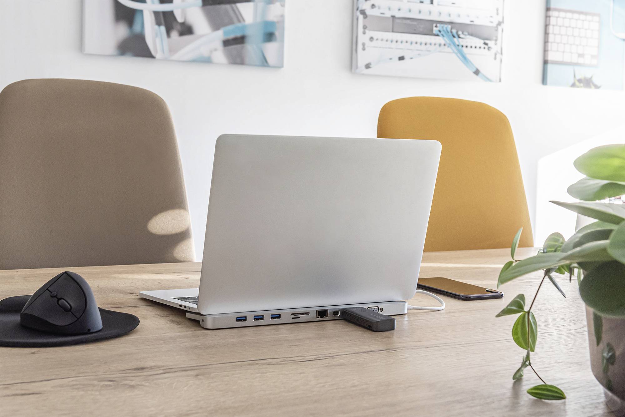 Un ordinateur portable est posé sur un bureau en bois entre deux chaises vides. À côté se trouvent une souris d'ordinateur et un smartphone.