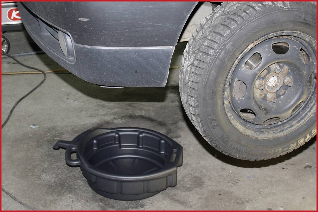 Une voiture est surélevée sur des chandelles, un bac de récupération d'huile est placé en dessous en préparation d'un changement d'huile dans un atelier de réparation.