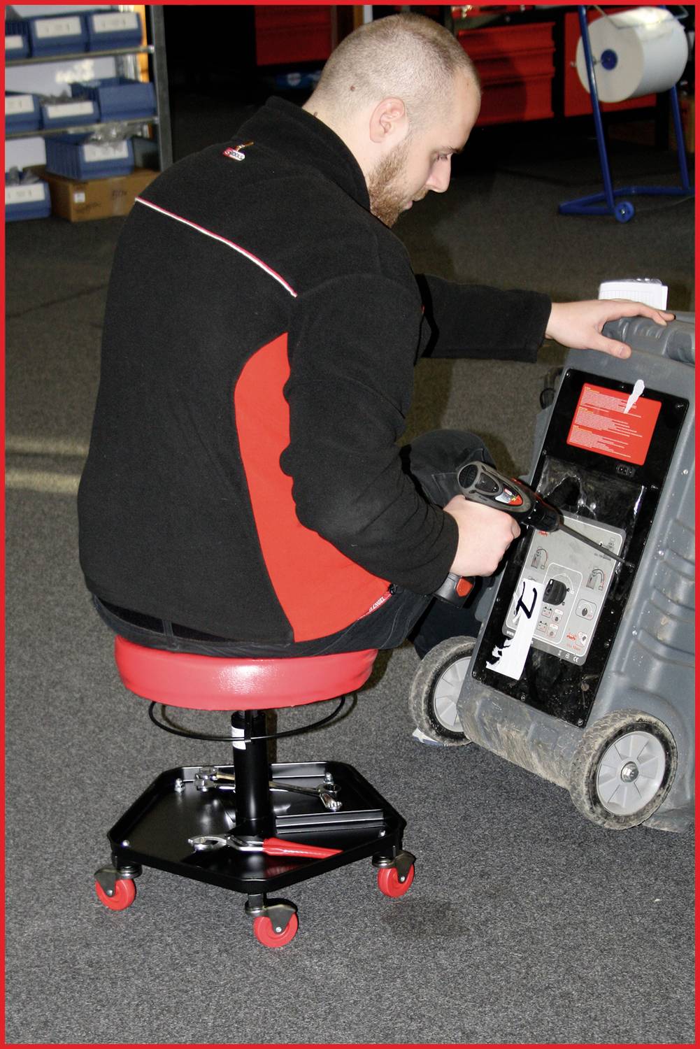 Un homme vérifie un appareil sur un siège mobile dans un entrepôt. Il tient un dispositif et examine l'avant du plus grand objet.