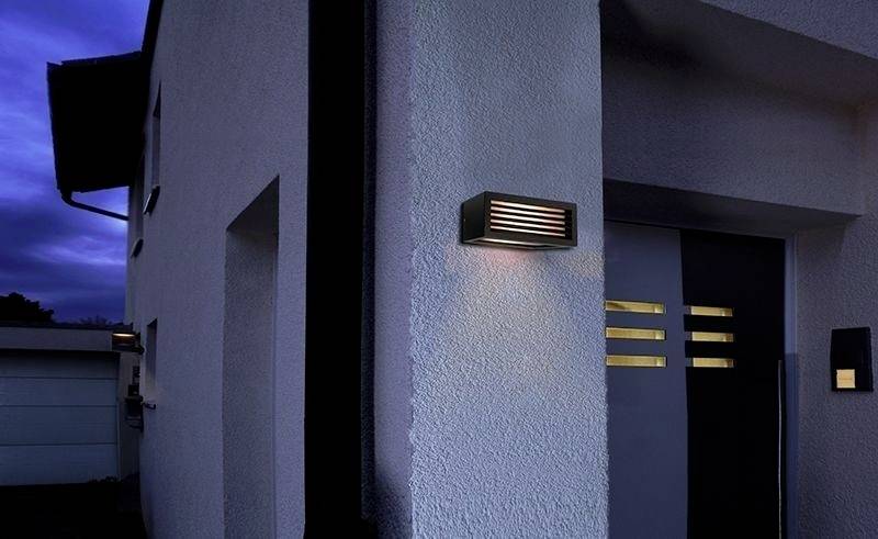 Éclairage extérieur à l'entrée d'une maison moderne au crépuscule, mettant en valeur la porte avec des lignes de décoration horizontales dorées.