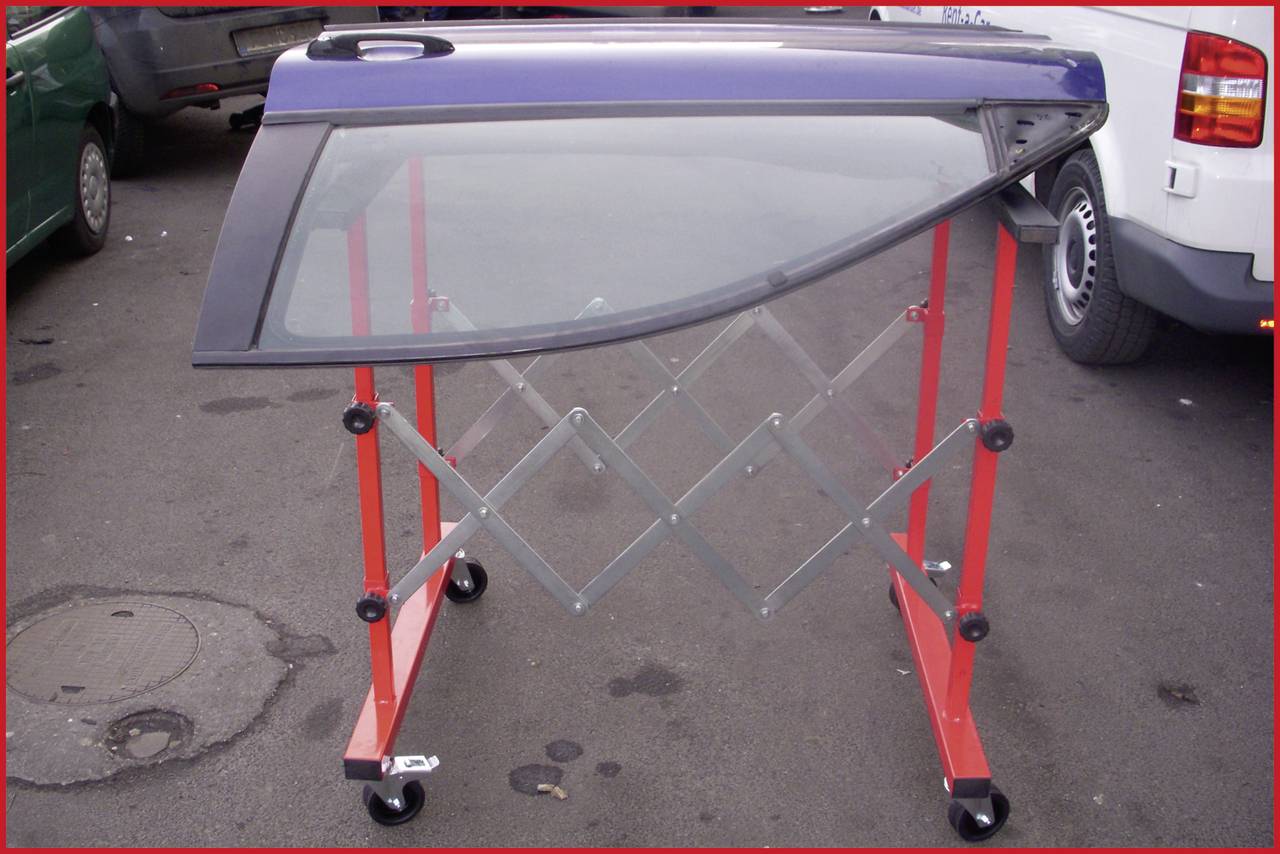 Porte de voiture sur un support rouge, placée pour séchage ou réparation sur un sol en asphalte dans un environnement d'atelier.