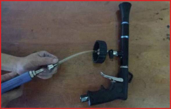 Une personne règle un appareil doté d'un tuyau en caoutchouc. L'appareil possède une poignée et un bouton de réglage, probablement un outil ou un composant de machine.