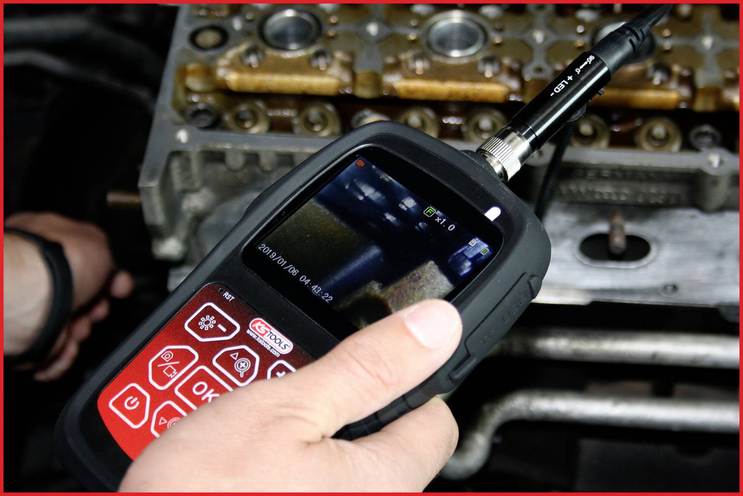 Une personne utilise un endoscope avec écran vidéo pour inspecter le moteur d'un véhicule. Le focus est mis sur l'appareil.