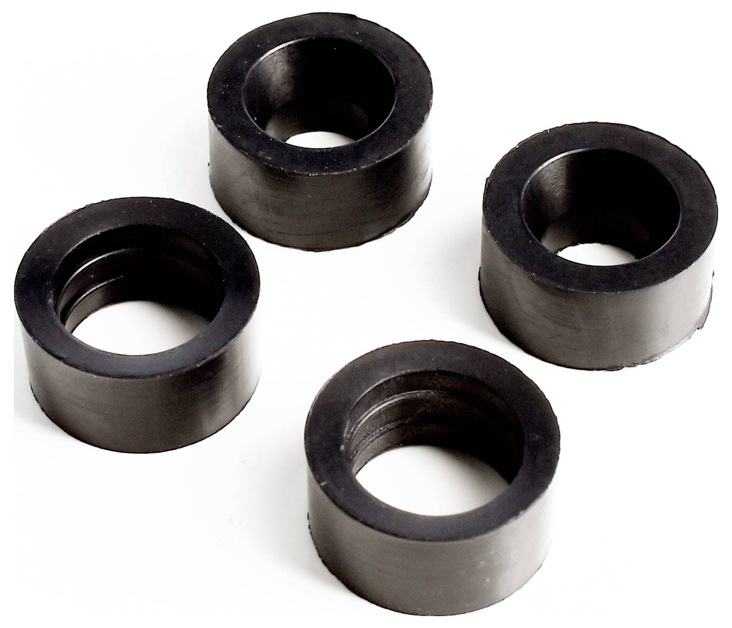 Quatre entretoises ou douilles cylindriques en caoutchouc noir disposées sur un fond blanc.