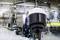 Caméra de surveillance au premier plan, installation de production industrielle en arrière-plan avec des machines et des chaînes de montage dans un environnement d'usine.