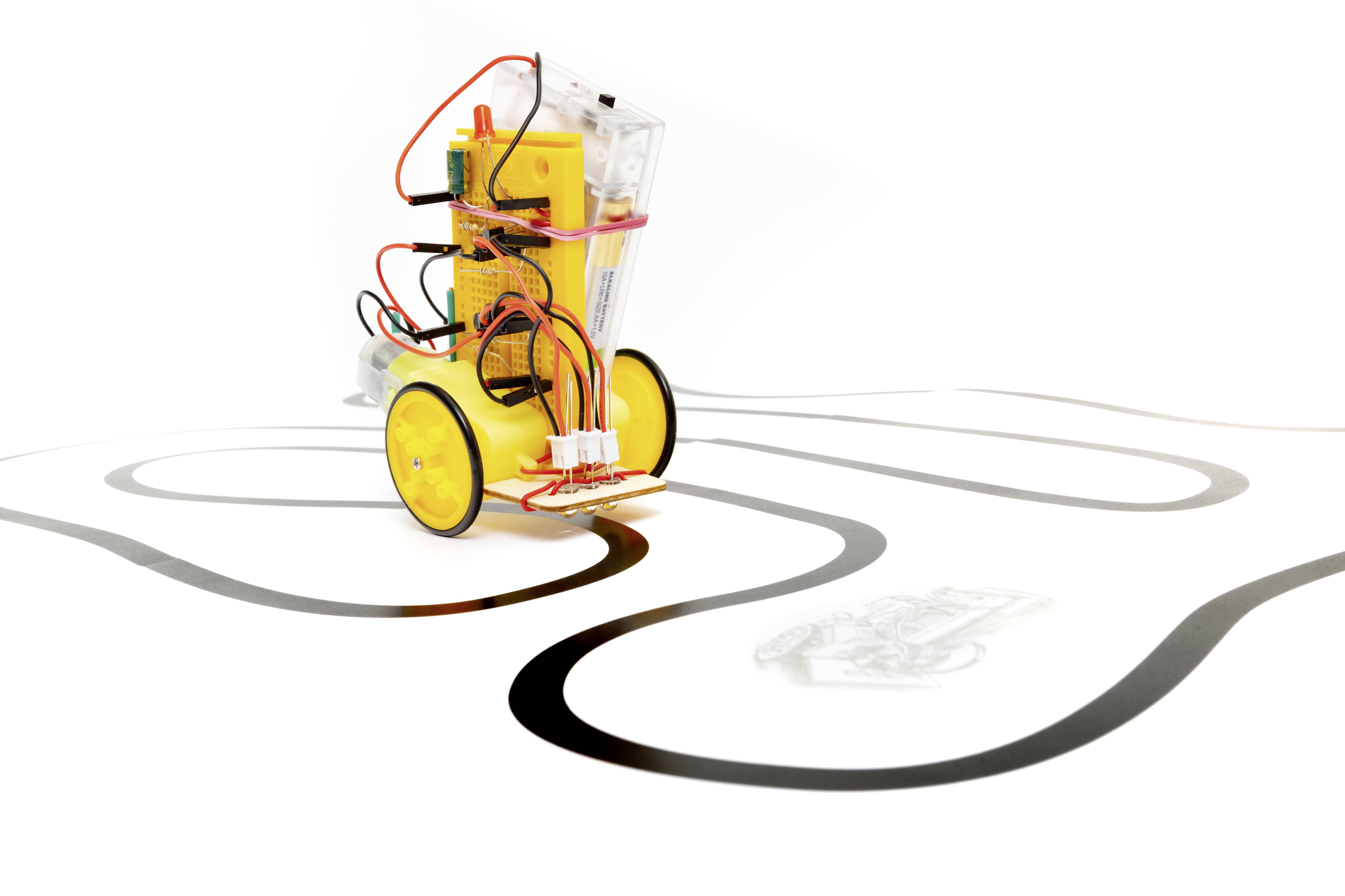 Un véhicule robotique jaune à deux roues suit une ligne noire sur une surface blanche. Des câbles et des capteurs sont visibles.