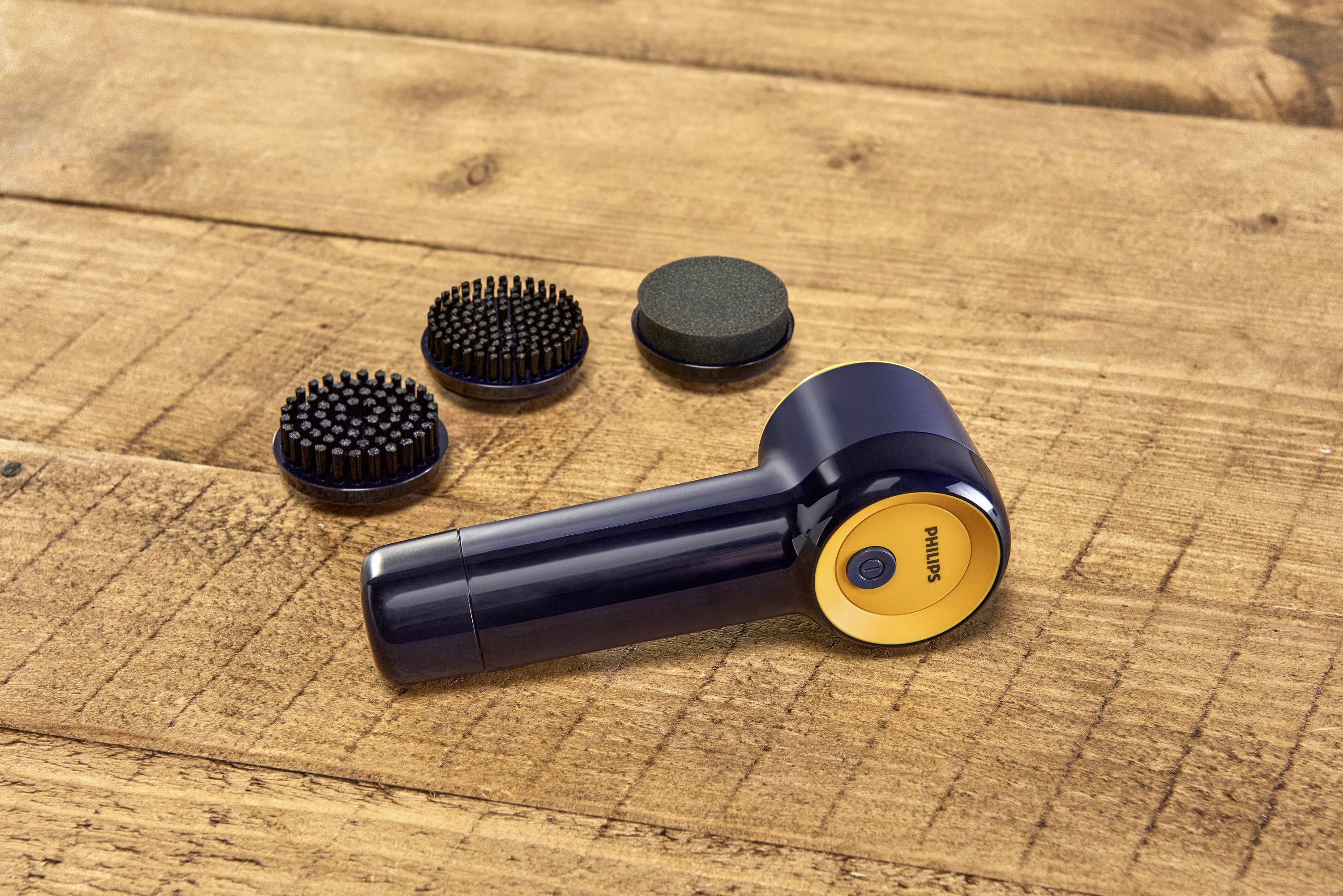 Un appareil de massage portable noir avec un accent jaune est posé sur une table en bois. Trois embouts interchangeables sont placés à côté.