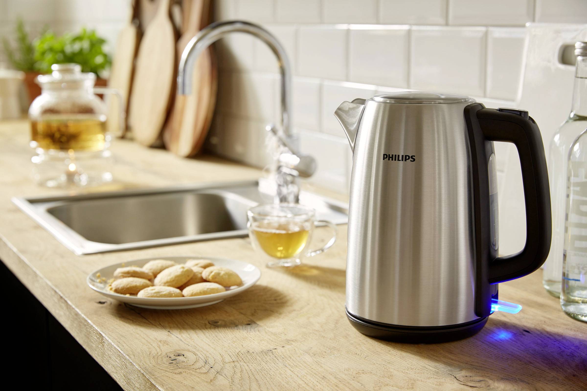 Bouilloire sur un plan de travail de cuisine à côté de biscuits et d'une tasse de thé. Un robinet et une théière sont visibles en arrière-plan.