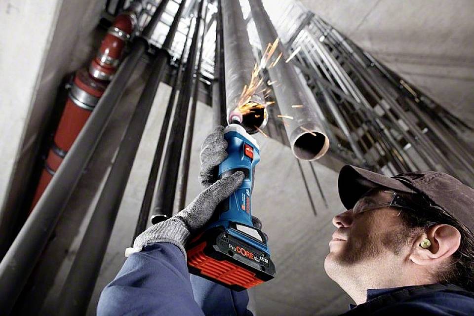 Une personne coupe un tuyau métallique avec un outil électrique. Des étincelles jaillissent du tuyau. Un équipement de protection est porté.