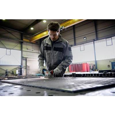 Un homme en tenue de travail ponçe du métal avec une meuleuse d'angle dans un atelier. Des étincelles volent de la disque métallique.