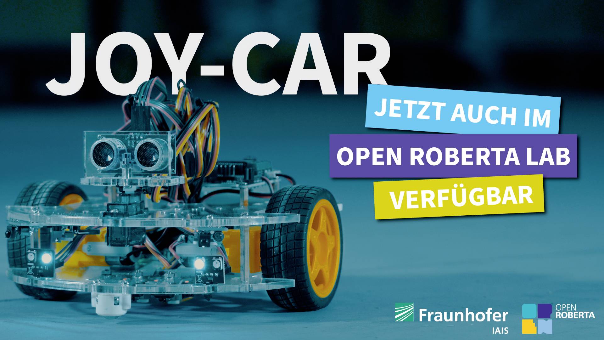 Un petit robot à roues, étiqueté 'JOY-CAR'. Texte : 'Maintenant disponible dans Open Roberta Lab'. Logos de Fraunhofer IAIS et Open Roberta.