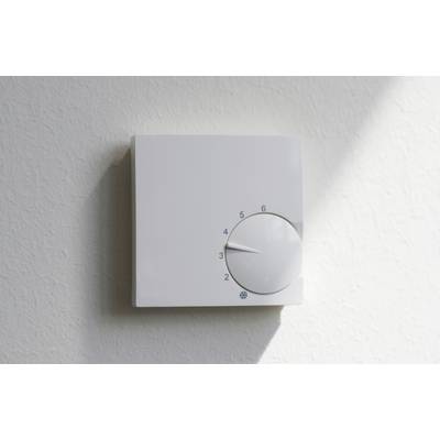 Un thermostat mural blanc avec bouton rotatif est réglé entre 3 et 4. La lumière du soleil entre par le côté droit.