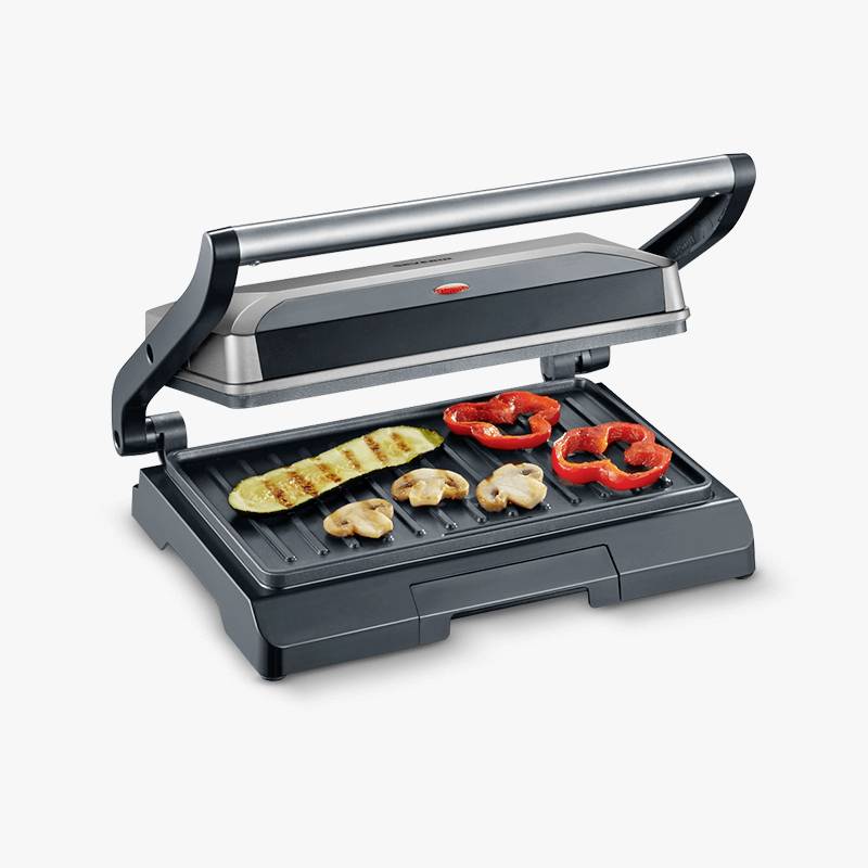 Un grill de table ouvert avec des légumes grillés, comprenant des courgettes, des poivrons et des champignons, sur la surface striée du grill.