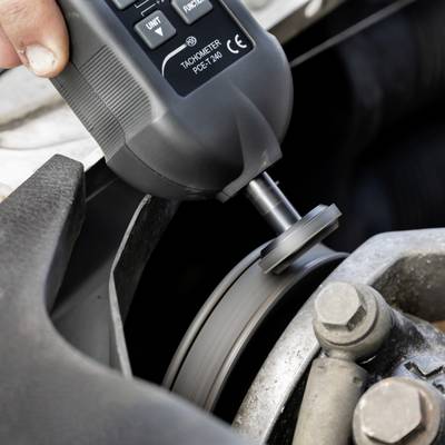 Une personne mesure la vitesse de rotation d'un objet en mouvement, probablement une pièce de machine, à l'aide d'un tachymètre.