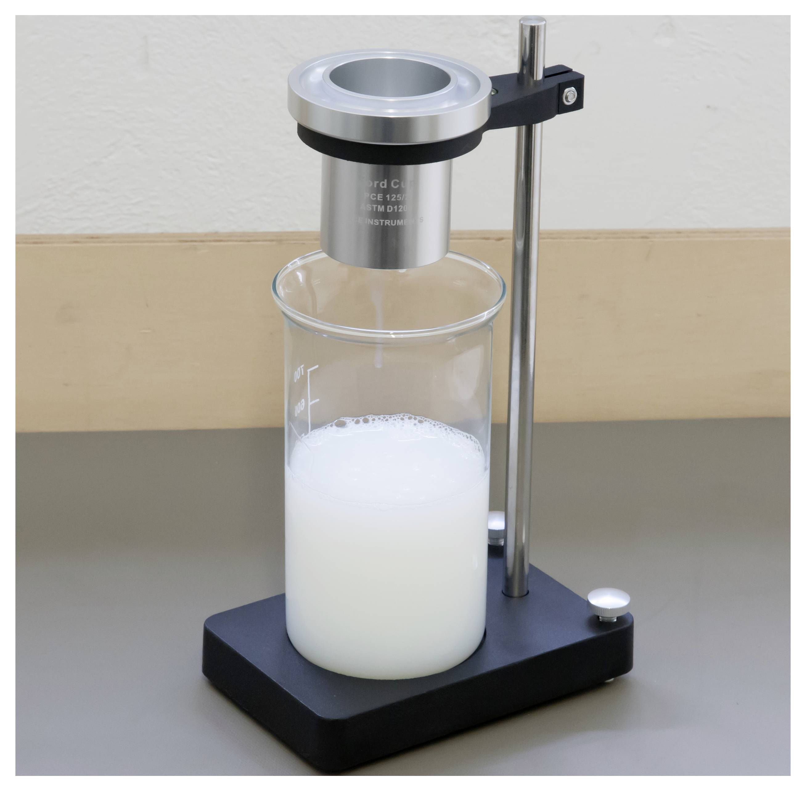 Viscosimètre de laboratoire avec une tige métallique suspendue au-dessus d'un bécher contenant un liquide blanc, mesurant la consistance du fluide.