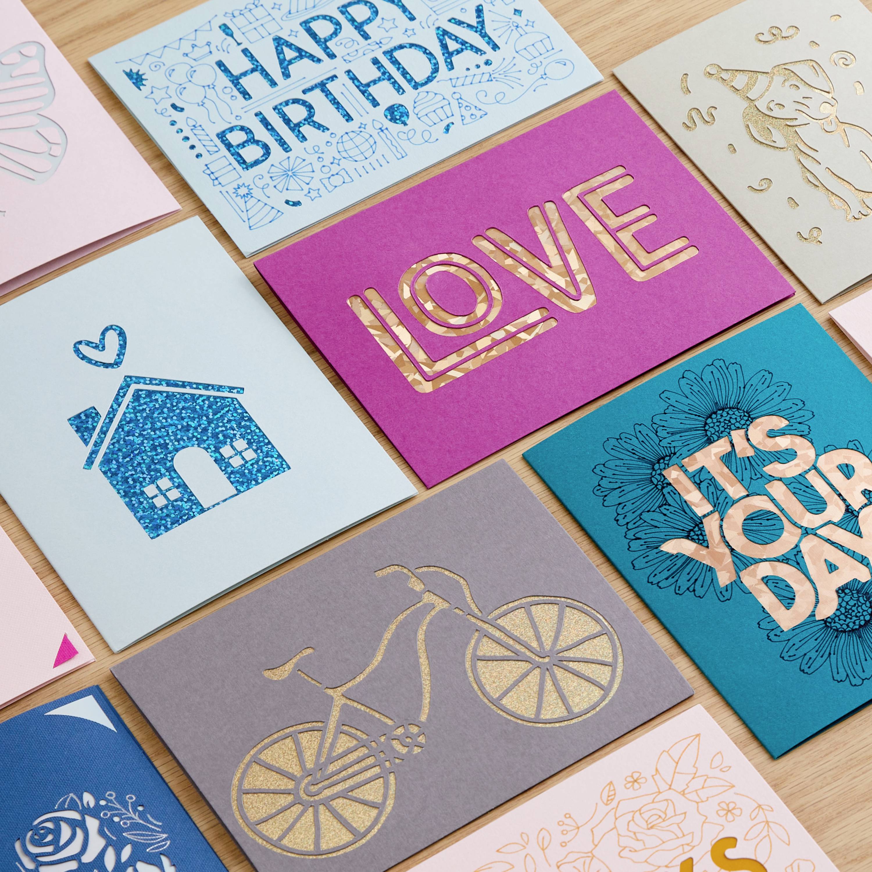 Différentes cartes de vœux sur une table, incluant des cartes 'Joyeux Anniversaire' et 'Amour', avec des designs colorés et dorés.