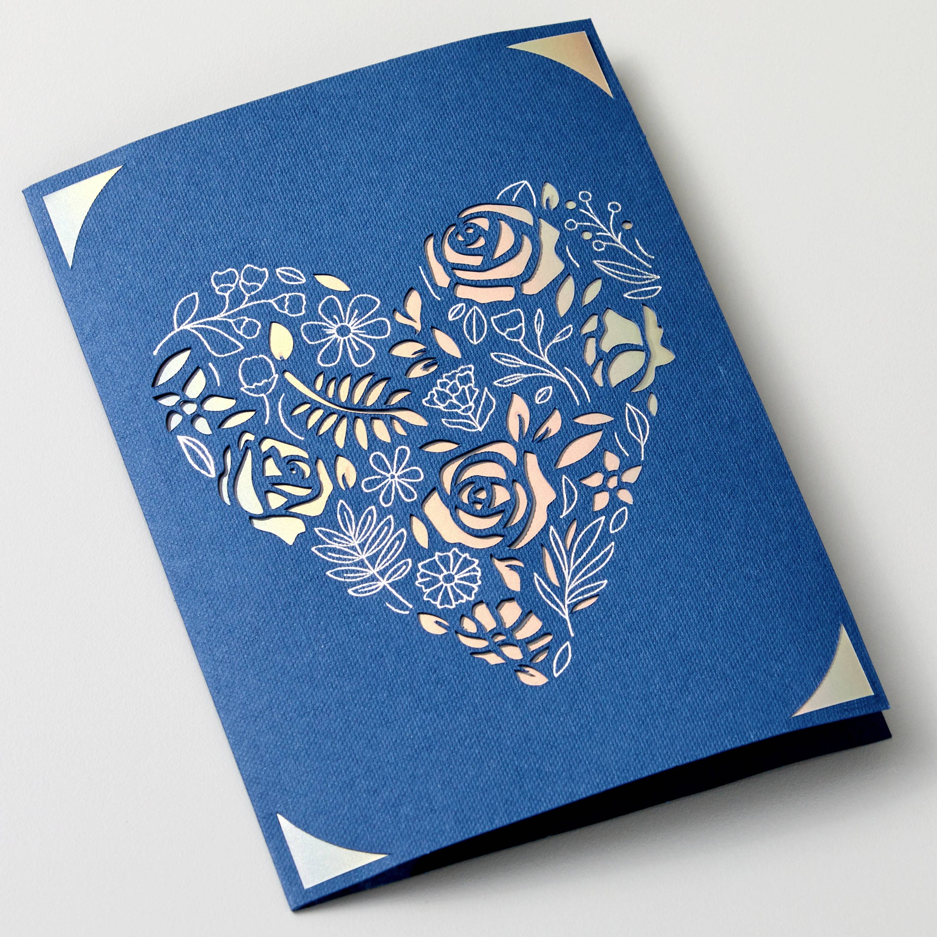 Une enveloppe bleue avec une découpe en forme de cœur à motif floral, présentant des fleurs et des feuilles.