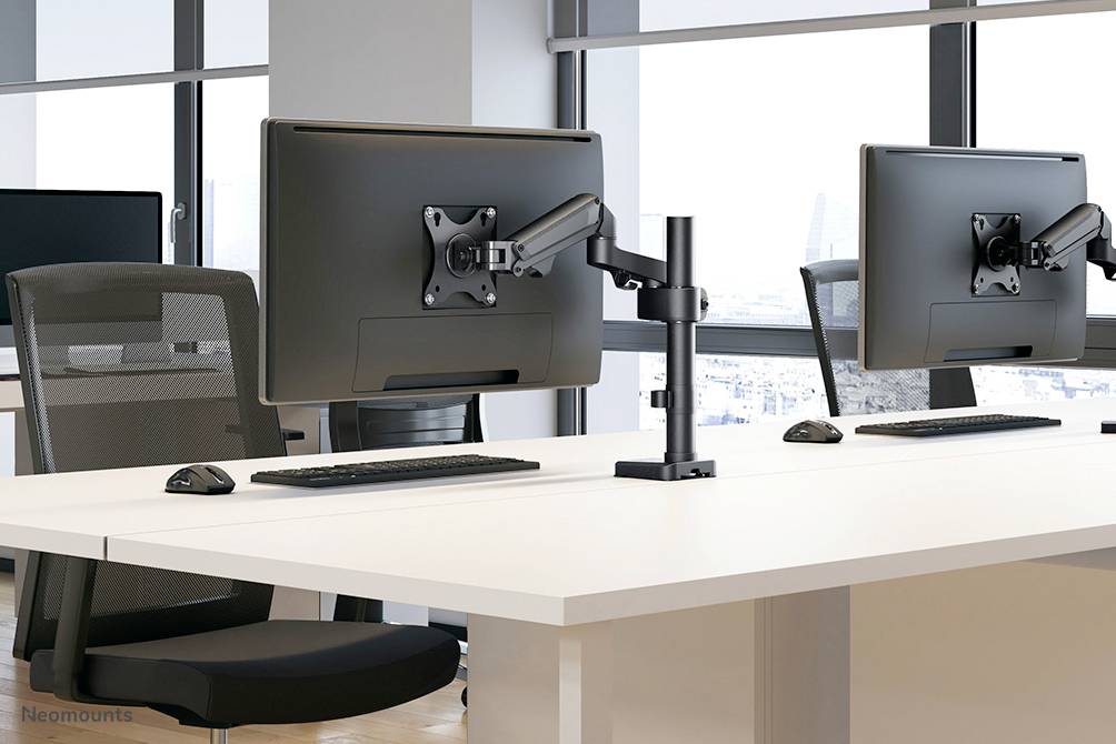 Deux moniteurs modernes sur des bureaux blancs dans un bureau avec de grandes fenêtres. Des chaises de bureau sont visibles à côté, dans un environnement lumineux et spacieux.