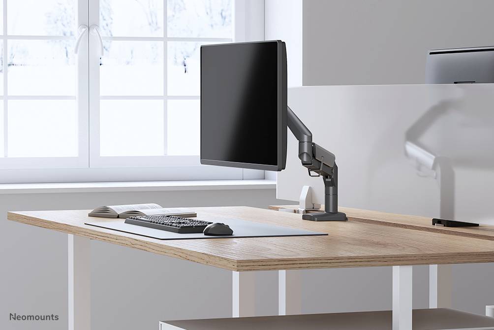 Un bureau moderne avec un bureau, un moniteur sur support, un clavier et une souris. De grandes fenêtres à l'arrière-plan laissent entrer la lumière.