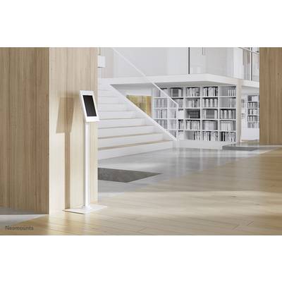 Une tablette posée sur un support est placée dans une pièce moderne et lumineuse, avec des parois en bois, un escalier et des étagères à livres en arrière-plan.