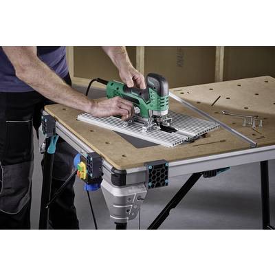Une personne travaille avec une scie sauteuse sur une table, découpant précisément le long d'un guide. Des vis et des outils sont posés à côté.