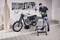 Un homme dans un atelier verse de l'huile dans une moto. Outils et accessoires accrochés au mur. Focus sur l'entretien de la moto.