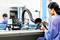 Une femme travaille avec un fer à souder sur une carte de circuit imprimé dans un laboratoire, avec un système d'aspiration et des outils en arrière-plan.