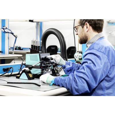 Une personne vêtue de bleu est assise à une table et manipule un appareil de soudure dans un environnement de laboratoire.