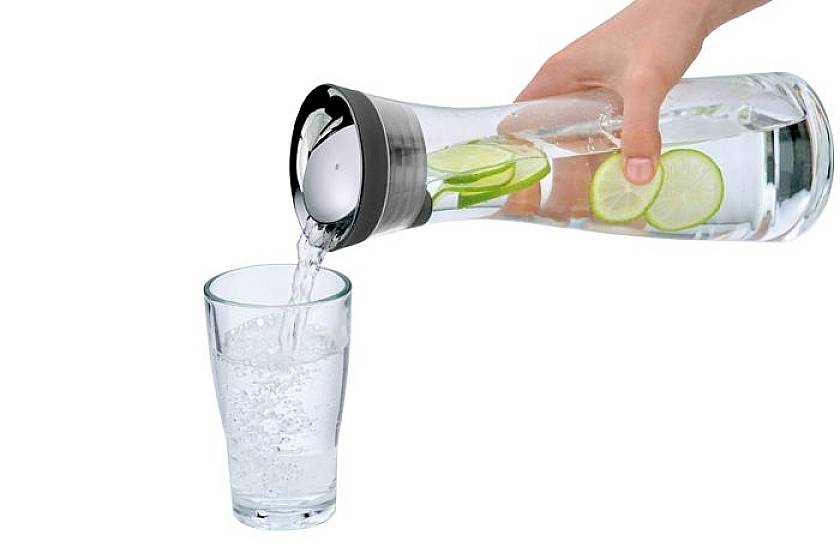 Une main verse de l'eau avec des tranches de citron vert d'une carafe dans un verre.