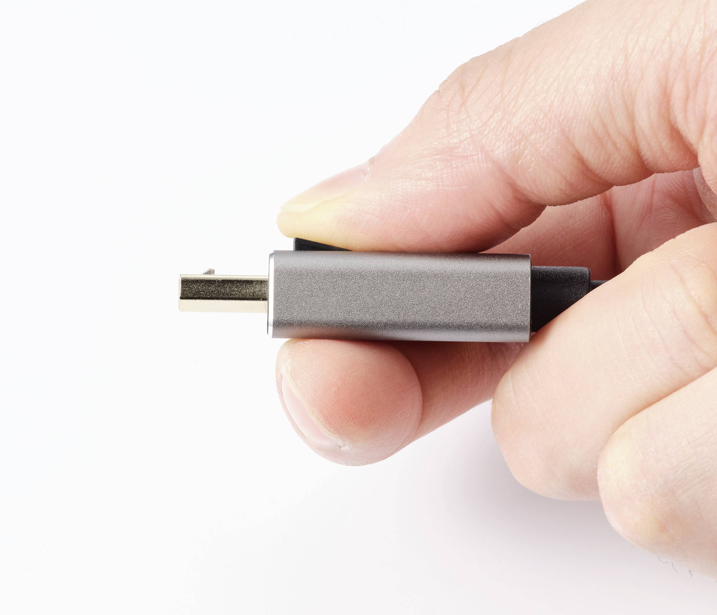 Une main tient un connecteur USB-C devant un fond blanc.