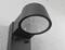 Un applique murale noir est fixé sur un mur gris. Elle présente un design moderne avec un abat-jour rond et une source lumineuse LED.