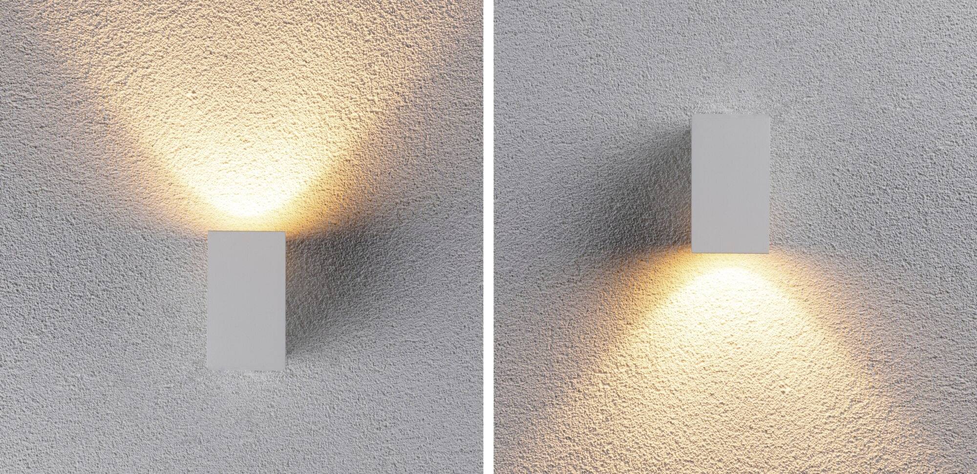 Lampe murale de gauche diffuse de la lumière vers le haut et vers le bas, lampe de droite uniquement vers le bas. Les deux sont montées sur un mur gris.
