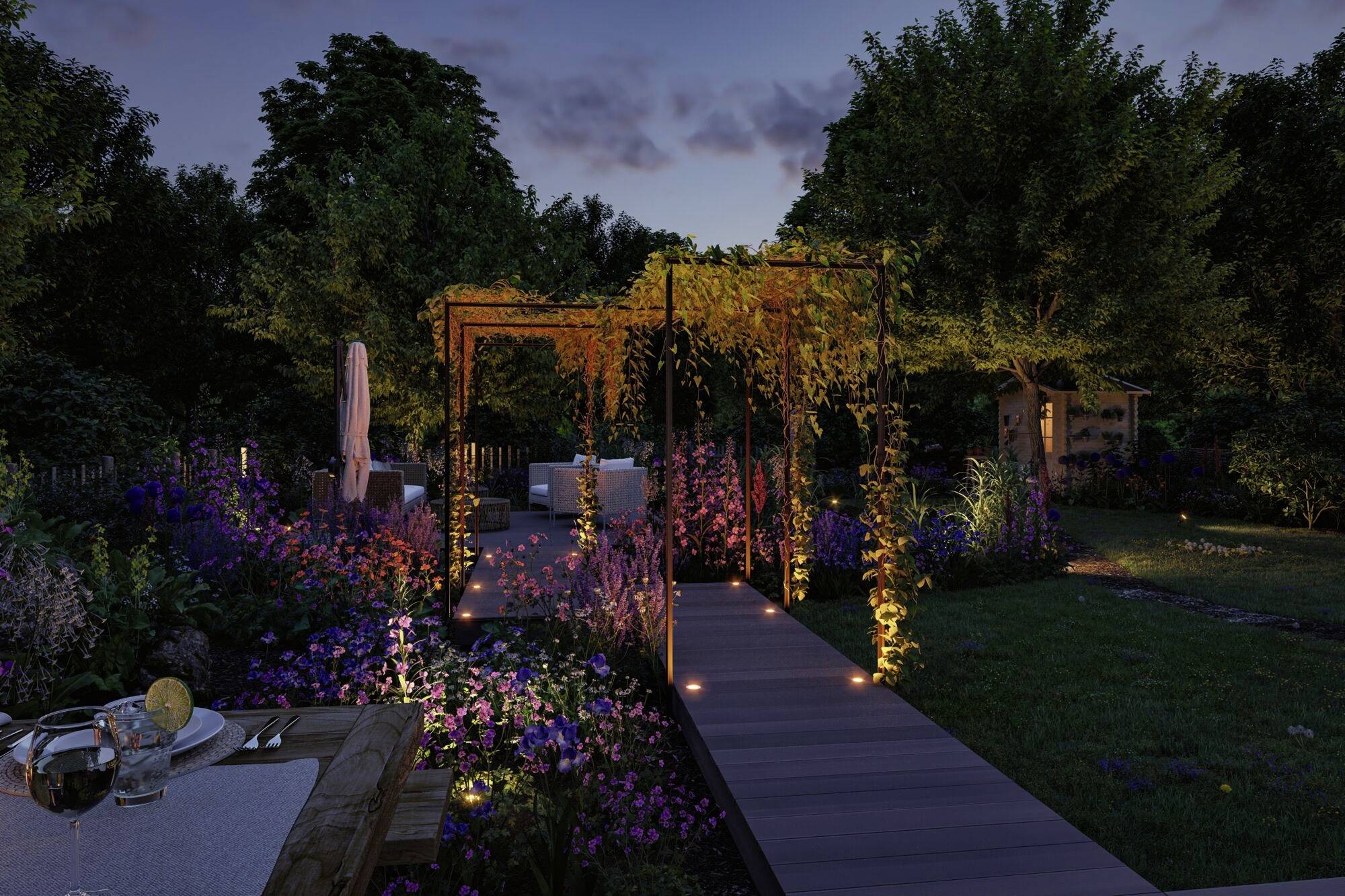 Un jardin éclairé au crépuscule avec des plantes en fleurs, une passerelle en bois et un espace de repos couvert sous une pergola envahie de végétation.