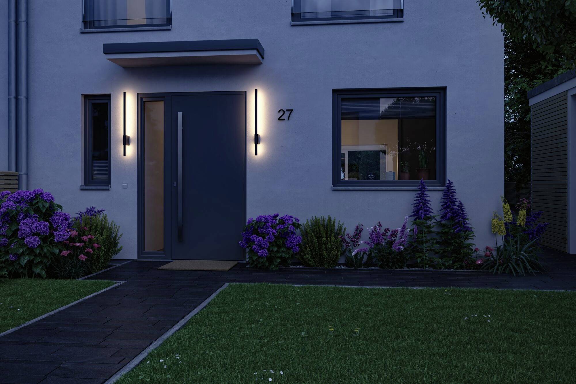 Entrée d'une maison moderne au crépuscule, avec un éclairage latéral et un jardin soigné rempli de fleurs colorées.