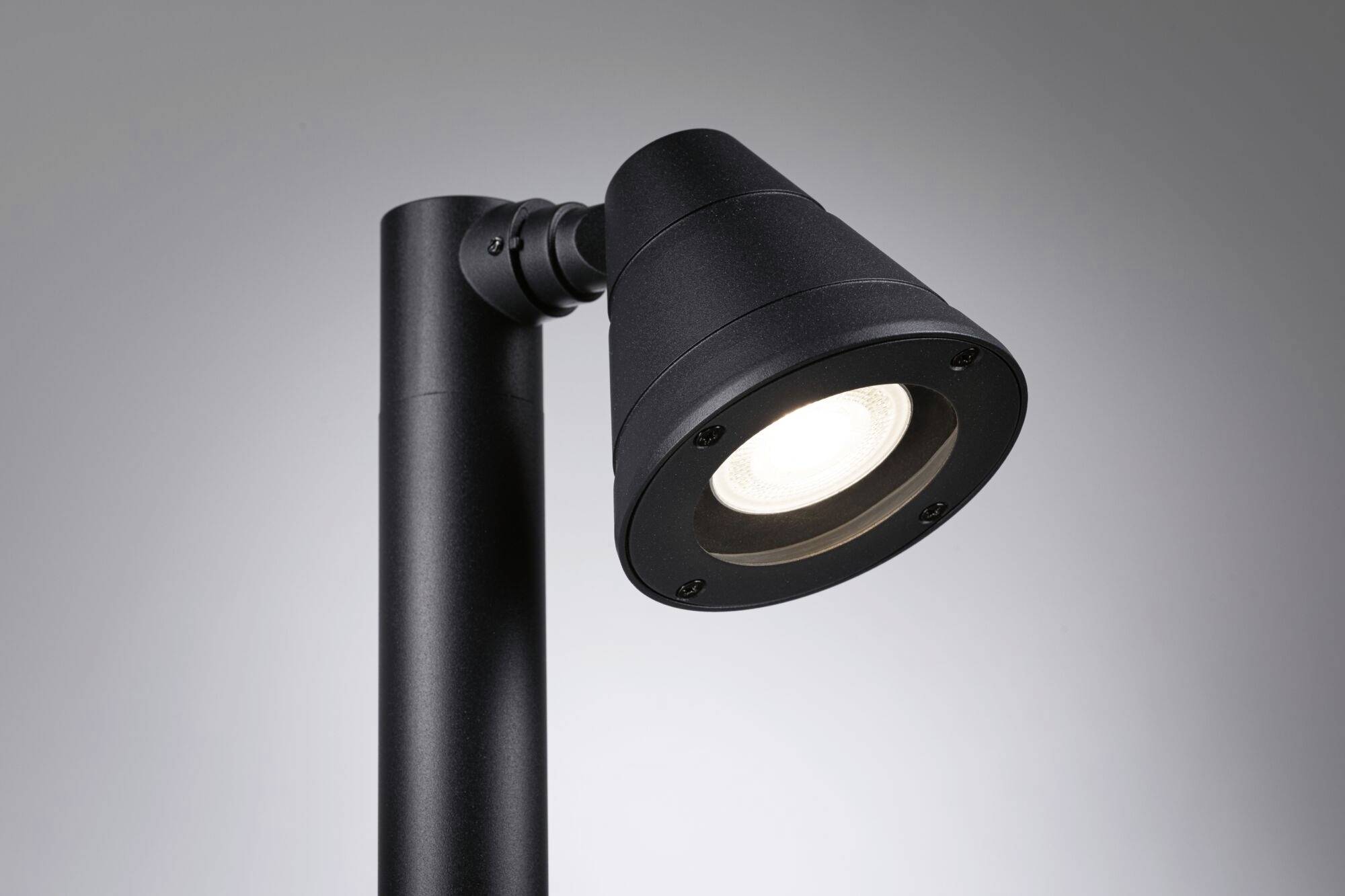 Un luminaire extérieur moderne noir avec un abat-jour conique diffuse une lumière vive et est représenté sur un fond neutre.