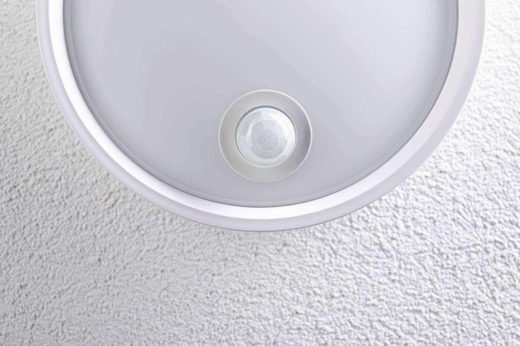 Plafonnier avec détecteur de mouvement intégré sur un plafond blanc à texture structurée.